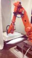 Orange six-axis industrial robot arm CNC milling a white foam block, producing fine chips
