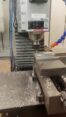 Vertical CNC milling machine face-milling an aluminum block with coolant and metal chips visible