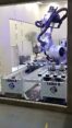 Six-axis industrial robot milling a circular metal workpiece inside a glass safety enclosure with visible metal chips