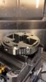 Vertical CNC milling machine machining an aluminum flange with coolant flow